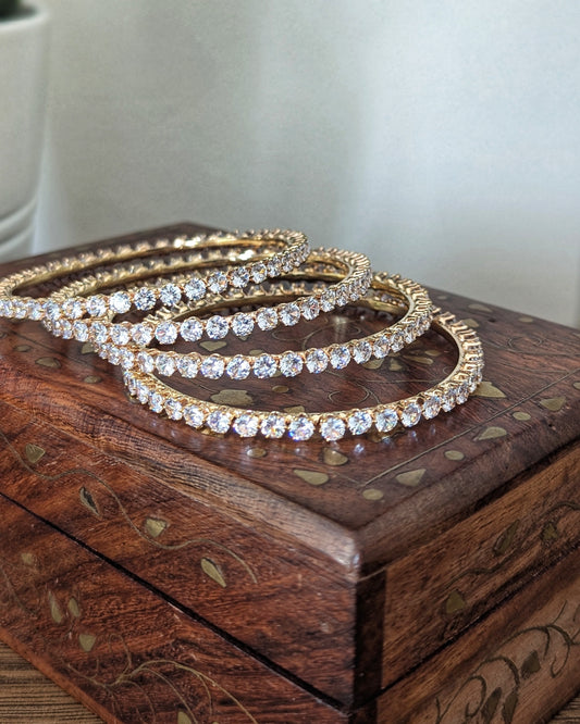 A set of four slim, gold-plated imitation bangles with a minimalist design and subtle sparkle. The bangles are stacked together on a soft fabric background, showcasing an everyday elegant style available at @sufnacanada. Pick-up in Ajax Ontario. Worldwide shipping available. Perfect for wedding, festival jewelry, indian Jewelry, kids jewelry, kundan jewelry, gifting, costume jewelry, fashion jewelry, Eid, onam, Diwali, karwachauth,