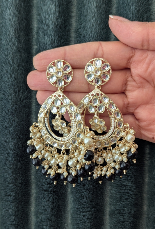 A pair of black and gold kundan chandbali earrings held in a hand, featuring intricate designs and drop-shaped stones. Available at Sufna Canada in Ajax, Durham Toronto GTA Ontario, worldwide shipping.