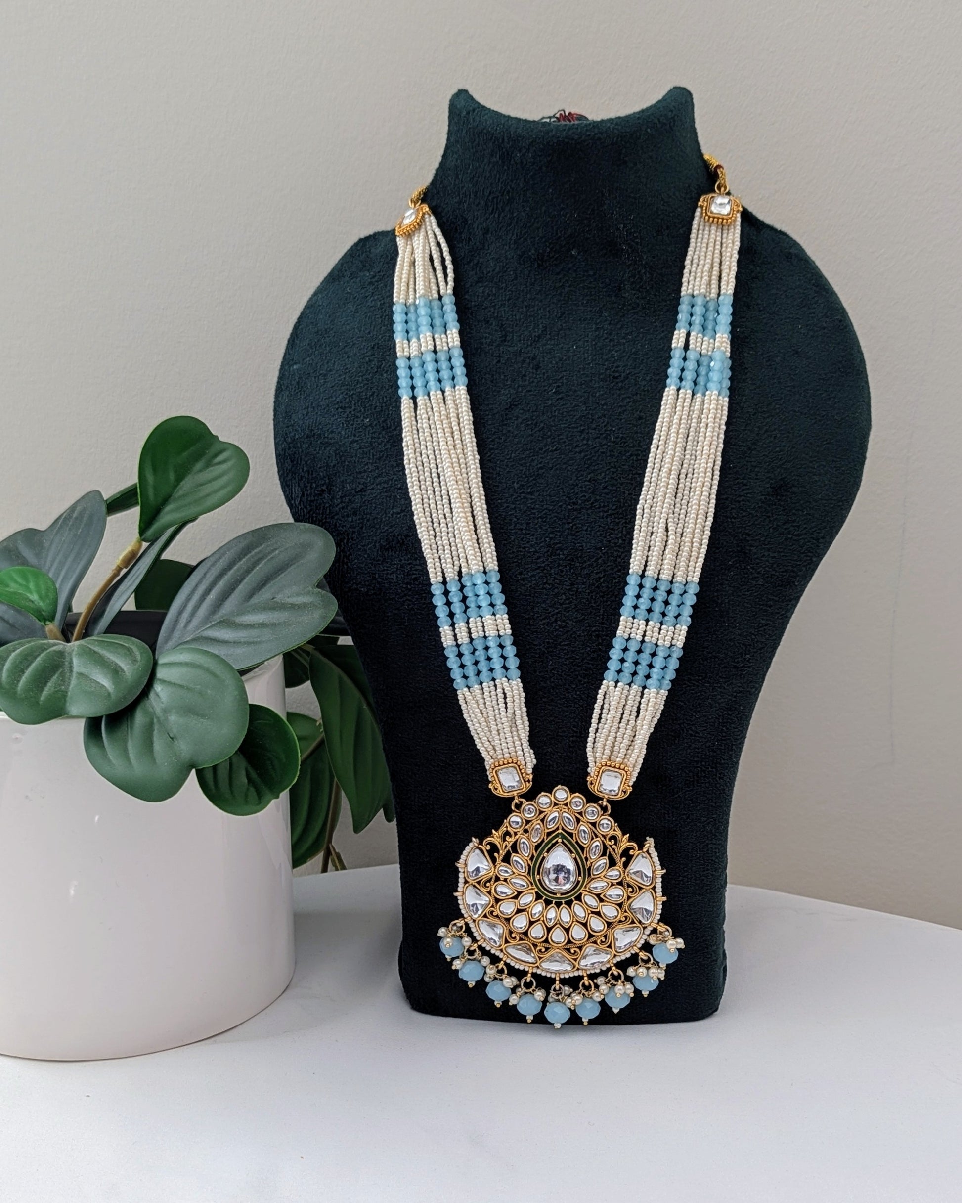 A baby blue and white pearl Kundan necklace with a large pendant displayed on a black mannequin bust, accompanied by matching earrings. Available for pickup in Ajax, Ontario and worldwide shipping.