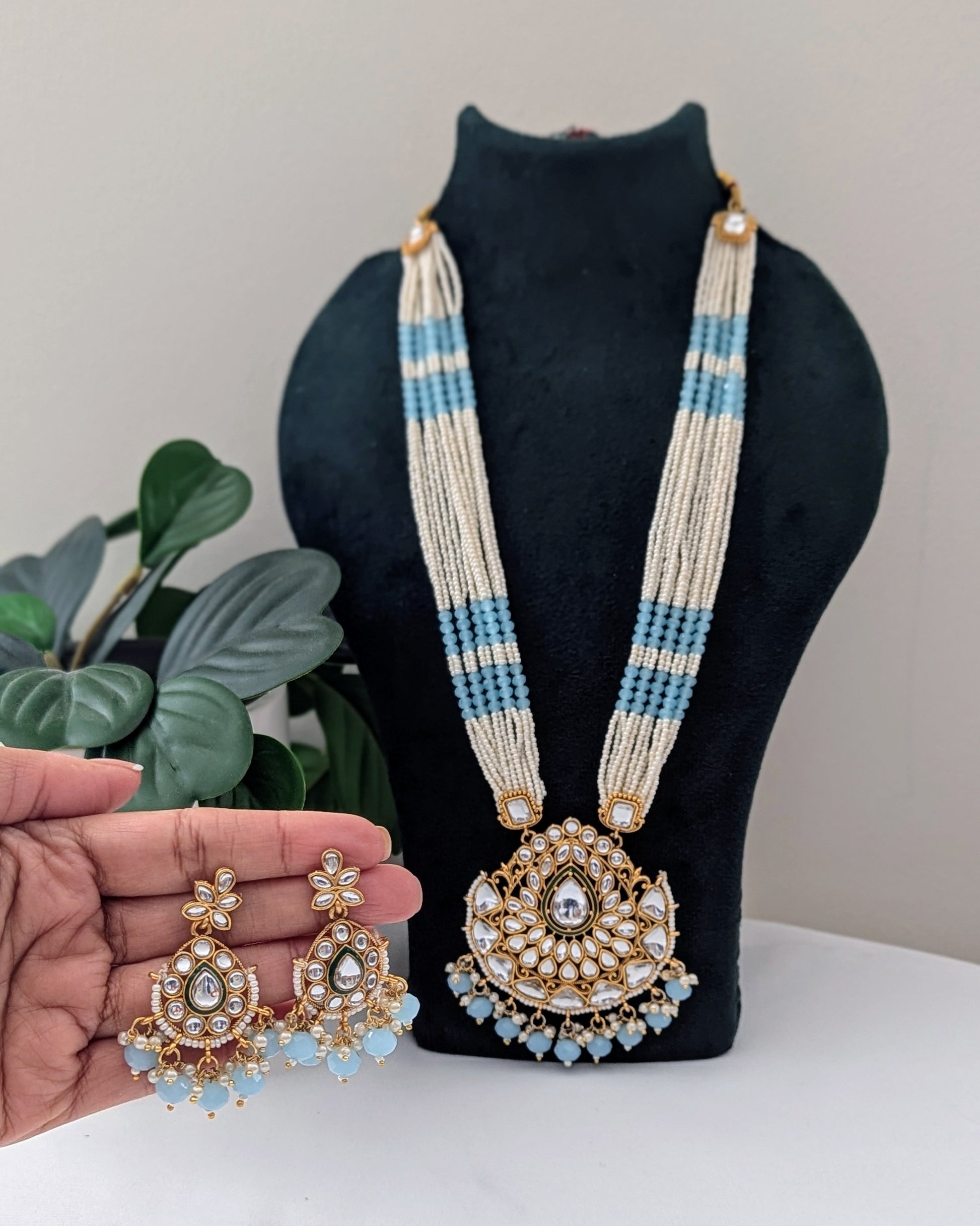 A baby blue and white pearl Kundan necklace with a large pendant displayed on a black mannequin bust, accompanied by matching earrings. Available for pickup in Ajax, Ontario and worldwide shipping.