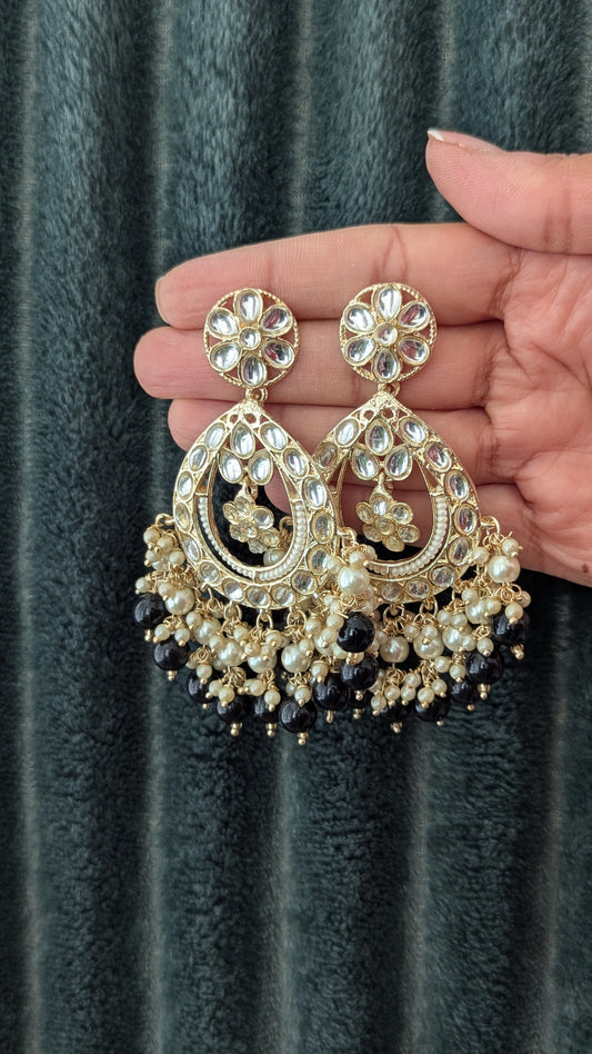 A pair of black and gold kundan chandbali earrings held in a hand, featuring intricate designs and drop-shaped stones. Available at Sufna Canada in Ajax, Durham Toronto GTA Ontario, worldwide shipping.