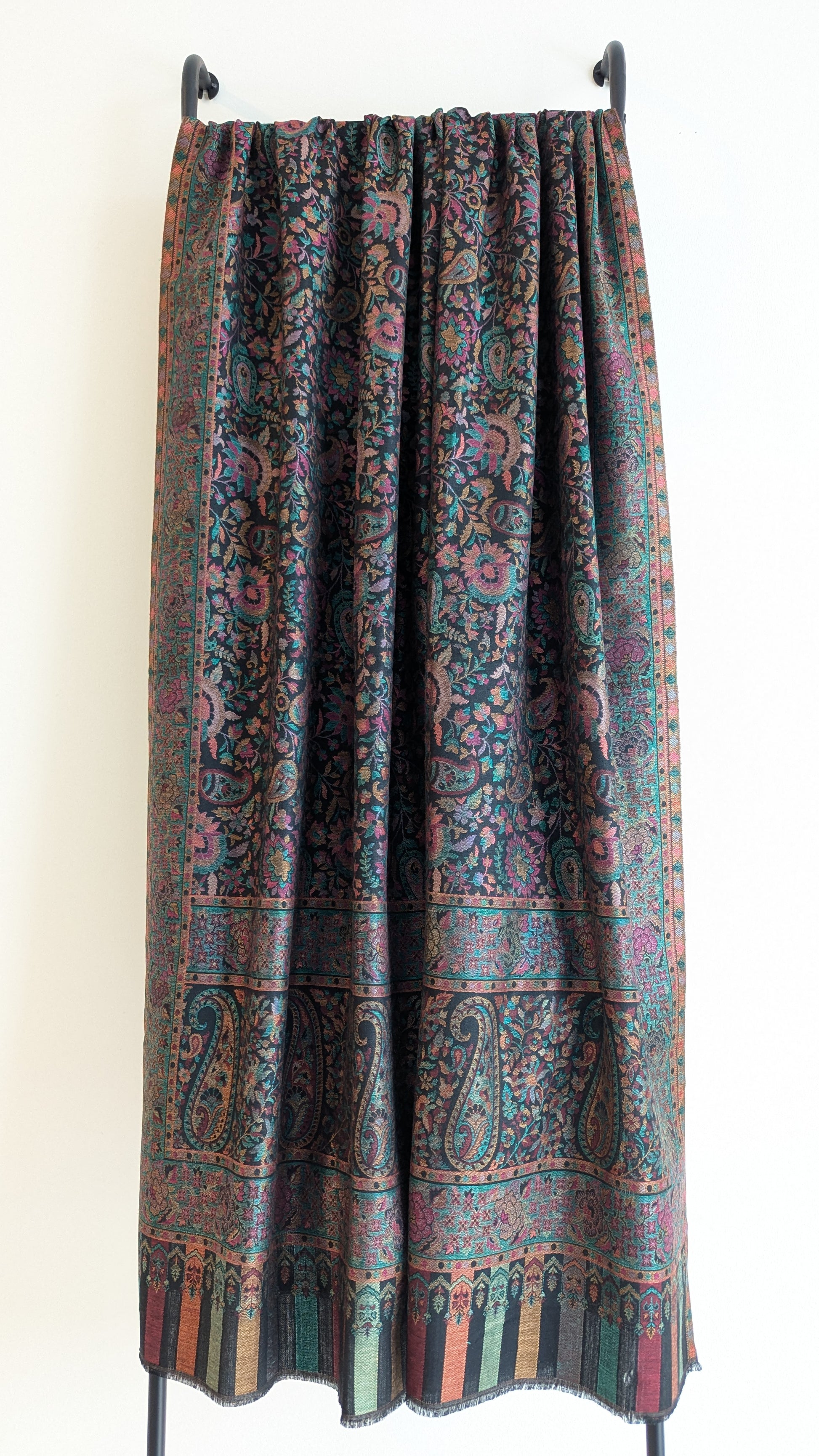 A black Kani lohi with multicolor floral and geometric patterns, displayed on a stand.