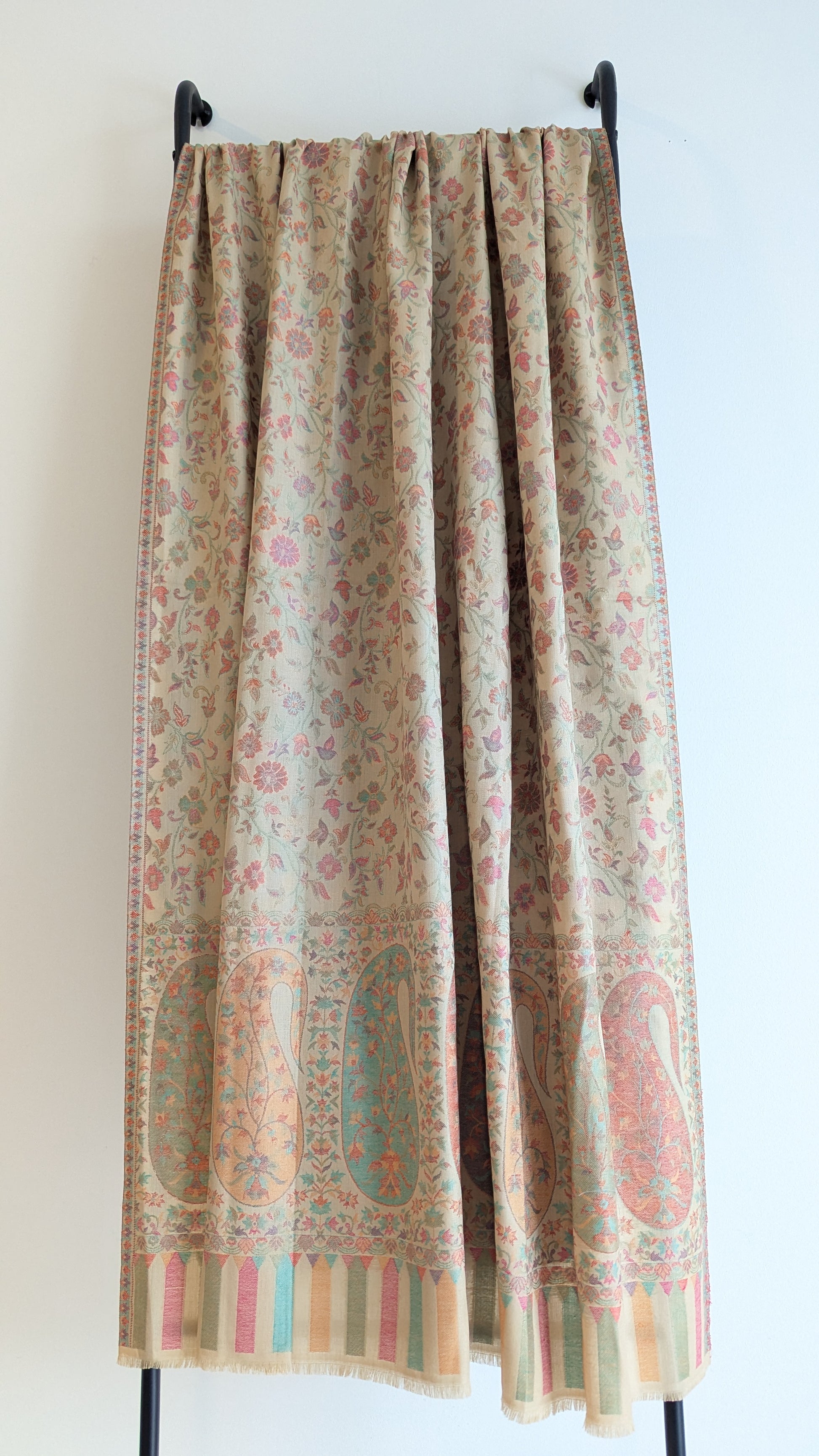 A beige shawl with multicolor patterns displayed.