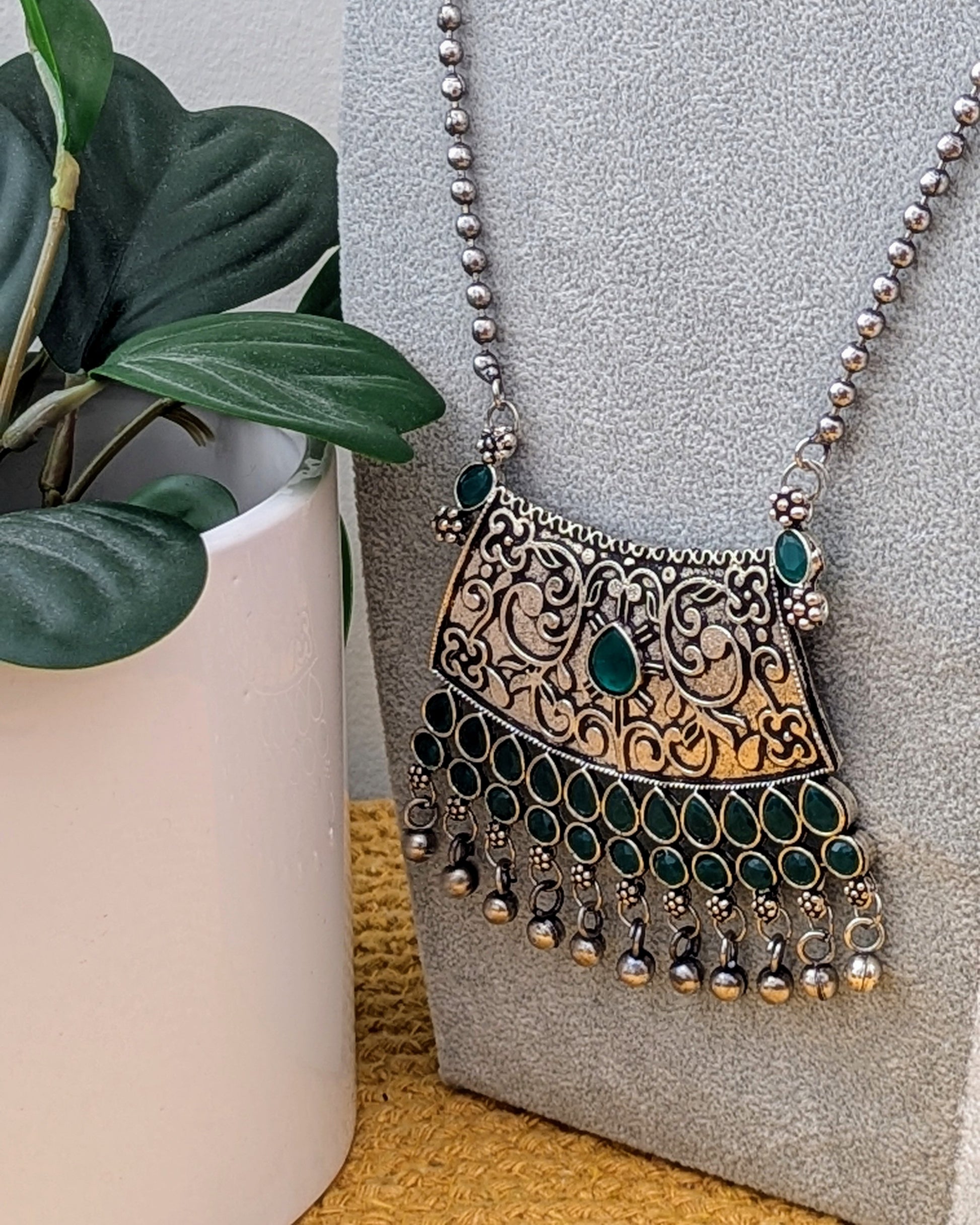 A person holding a green oxidized silver long necklace with a statement pendant, alongside matching earrings, displayed on a mannequin bust. Pick-up in Ajax Ontario. Worldwide shipping available. Perfect for weddings, festival jewelry, indian Jewelry, kids jewelry, kundan jewelry, gifting, costume jewelry, fashion jewelry, Eid, onam, Diwali, karwachauth, navratri. Free shipping available. Jewelry for women. Indian jewelry in ajax toronto canada