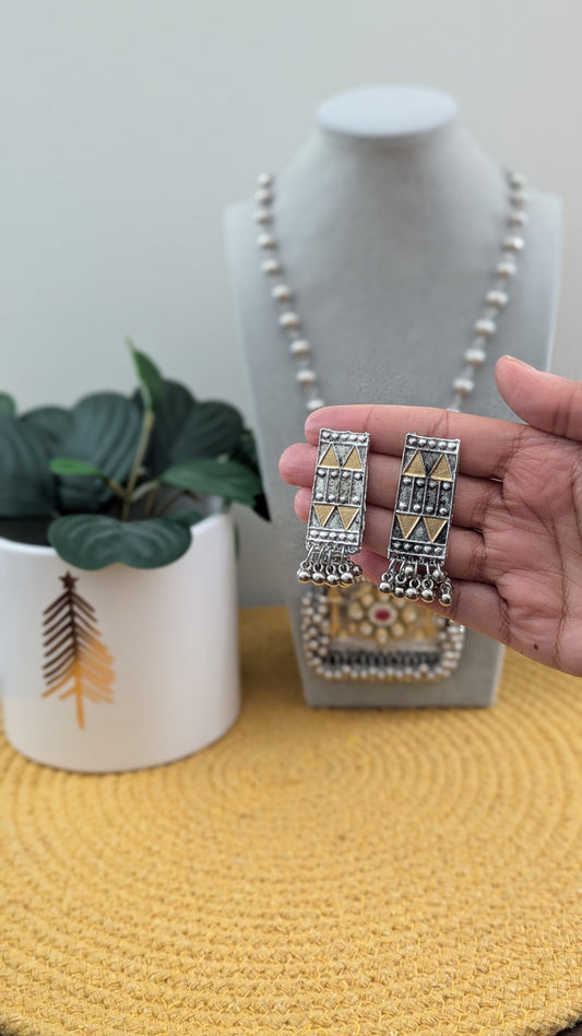 Oxidized silver long necklace with a statement pendant displayed on a mannequin, accompanied by matching earrings, against a white background with a plant to the side.