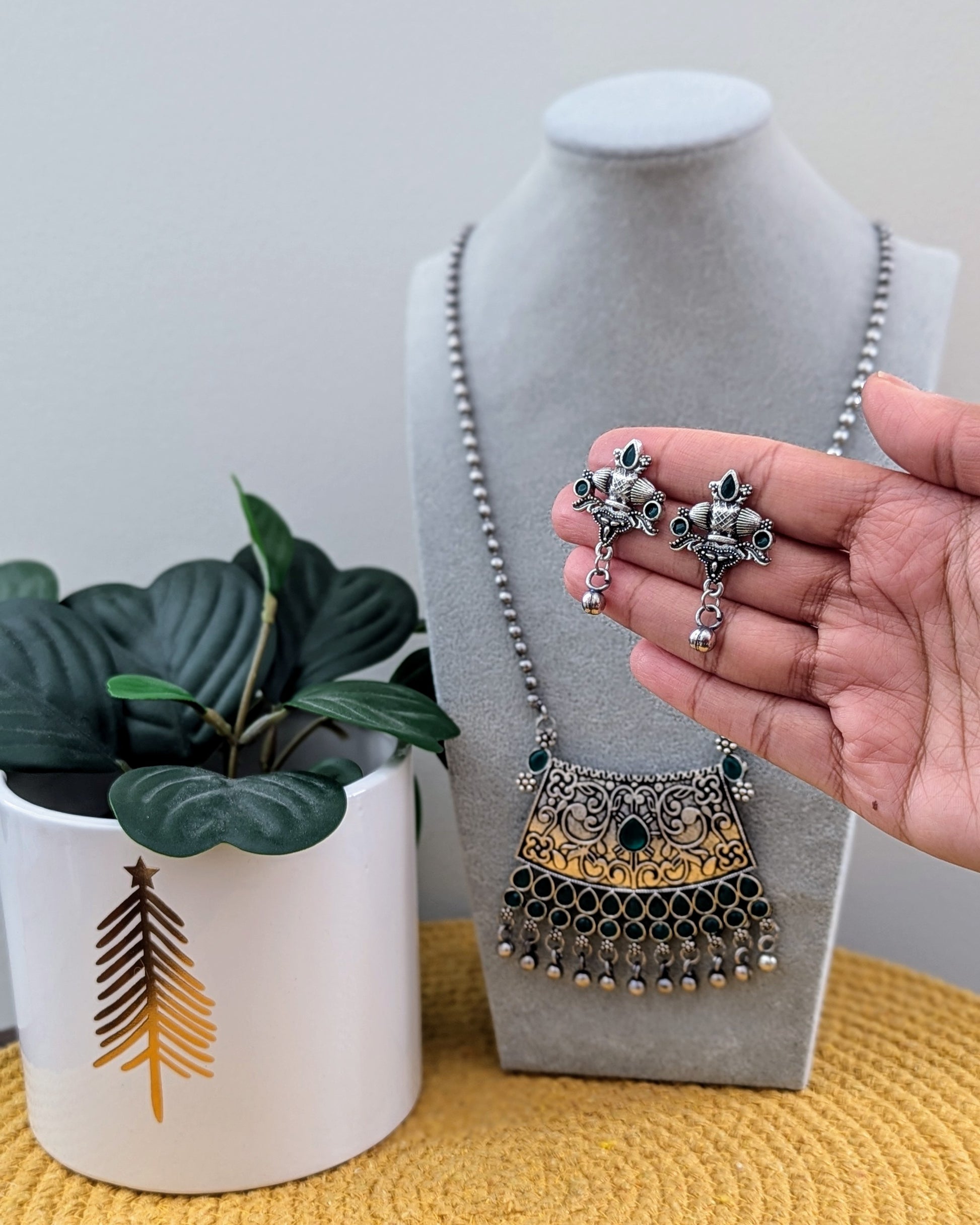 A person holding a green oxidized silver long necklace with a statement pendant, alongside matching earrings, displayed on a mannequin bust. Pick-up in Ajax Ontario. Worldwide shipping available. Perfect for weddings, festival jewelry, indian Jewelry, kids jewelry, kundan jewelry, gifting, costume jewelry, fashion jewelry, Eid, onam, Diwali, karwachauth, navratri. Free shipping available. Jewelry for women. Indian jewelry in ajax toronto canada