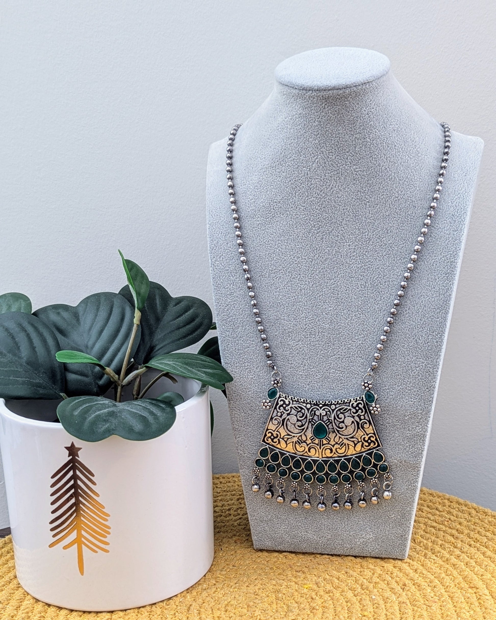 A person holding a green oxidized silver long necklace with a statement pendant, alongside matching earrings, displayed on a mannequin bust. Pick-up in Ajax Ontario. Worldwide shipping available. Perfect for weddings, festival jewelry, indian Jewelry, kids jewelry, kundan jewelry, gifting, costume jewelry, fashion jewelry, Eid, onam, Diwali, karwachauth, navratri. Free shipping available. Jewelry for women. Indian jewelry in ajax toronto canada