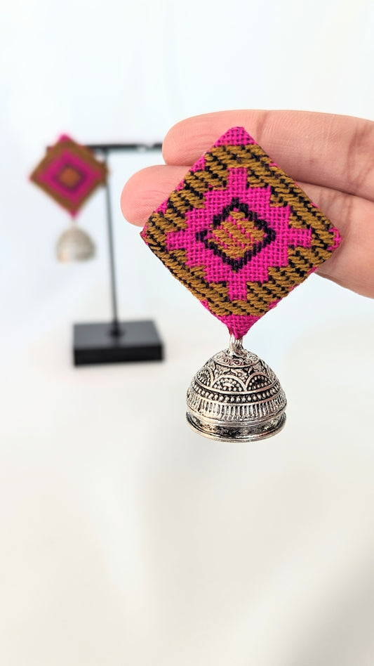 A pair of pink ikat fabric earrings displayed on a stand, with the earrings featuring a geometric pattern and silver-colored bell-like attachments. Pick-up in Ajax Ontario. Worldwide shipping available. Perfect for wedding, festival jewelry, indian Jewelry, kids jewelry, kundan jewelry, gifting, costume jewelry, fashion jewelry, Eid, onam, Diwali, karwachauth, navratri. Free shipping available. Jewelry for women. Indian jewelry in ajax durham region.