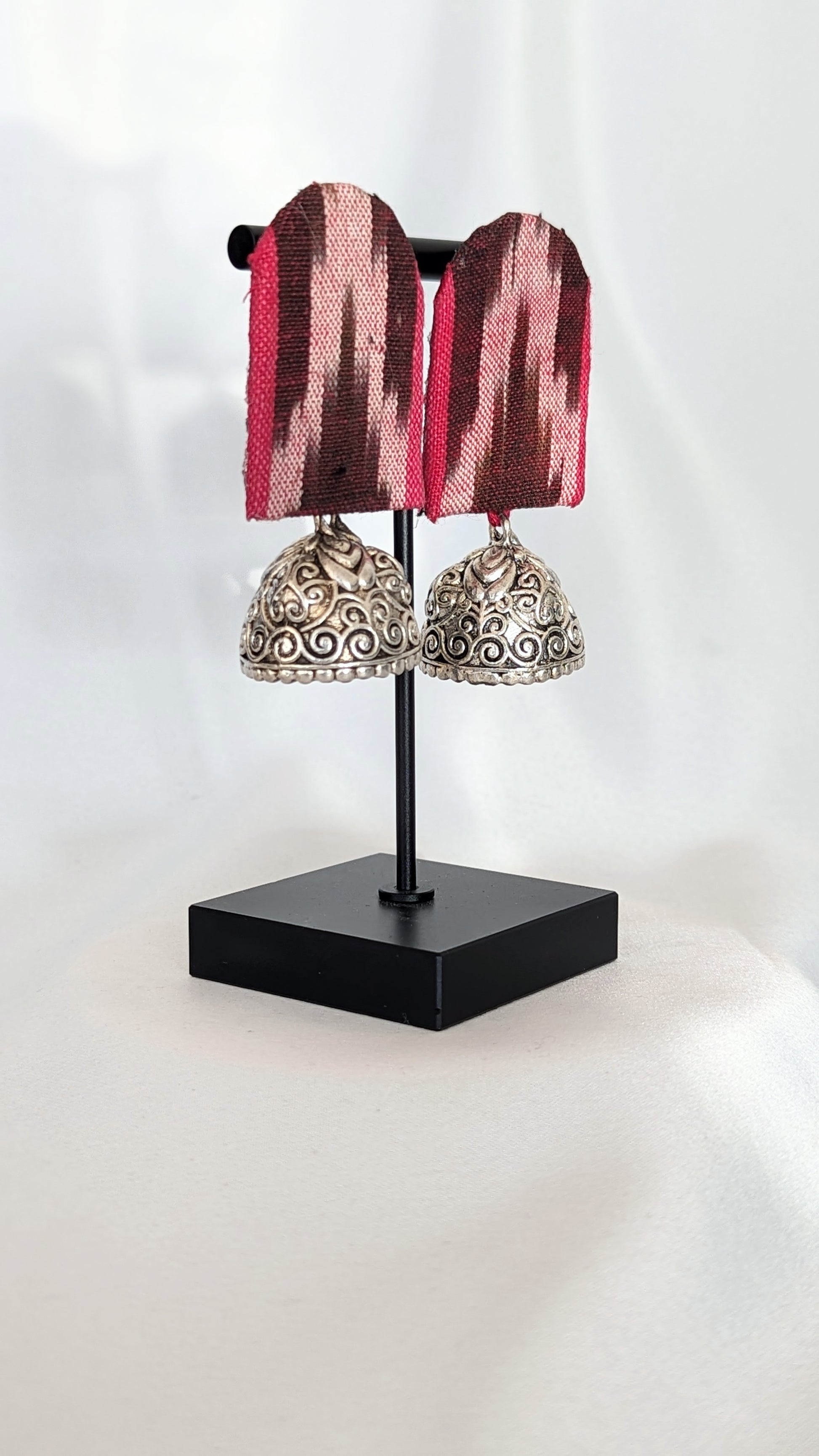 A pair of maroon and pink striped ikat fabric earrings displayed on a stand.