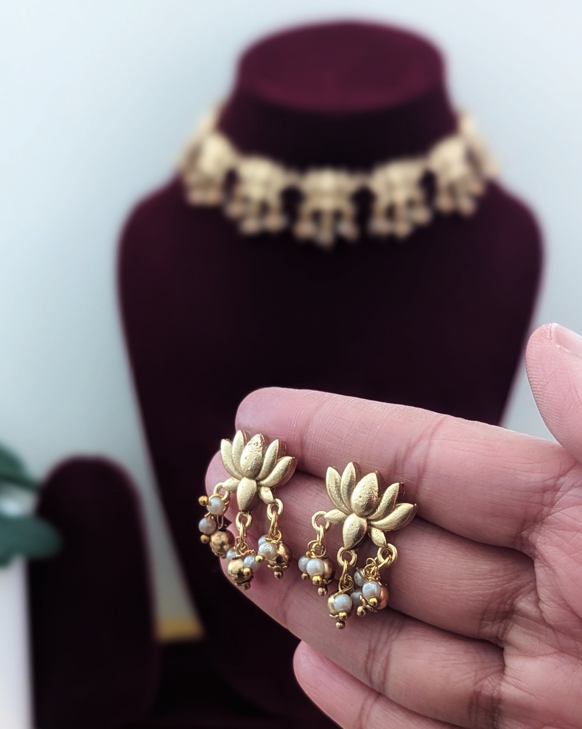 A gold-colored necklace with lotus flower designs displayed on a red velvet mannequin.