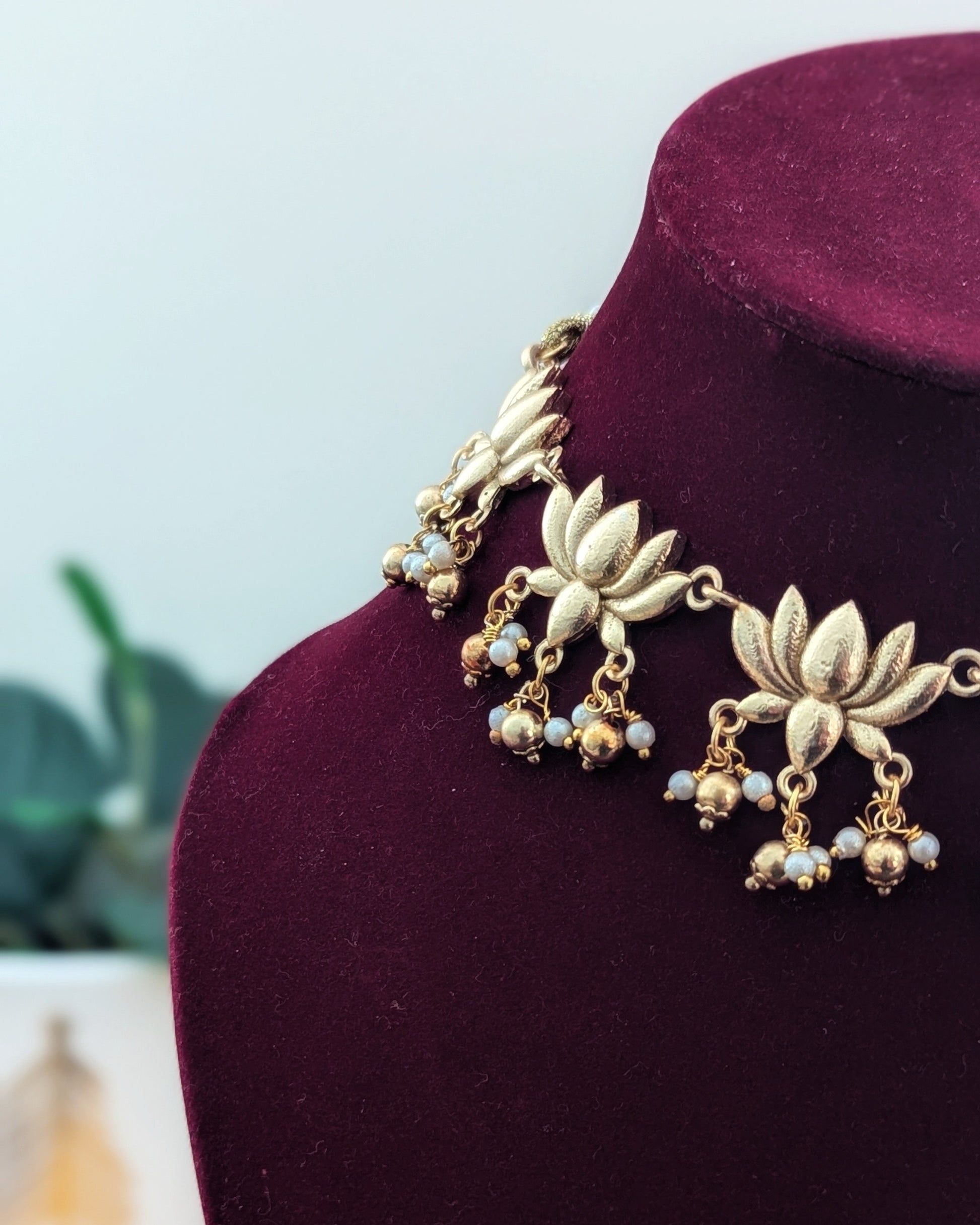 A gold-colored necklace with lotus flower designs displayed on a red velvet mannequin.